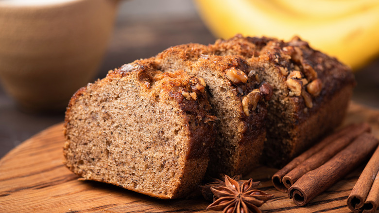 A sliced loaf of spiced banana bread with cinnamon sticks and star anise surrounding it