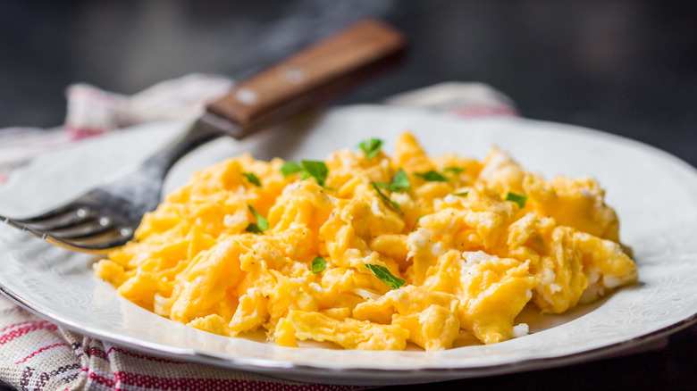 Scrambled eggs are topped with chives and served on a plate.