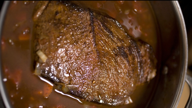 Brisket braising in a pot of brown liquid with some visible carrots