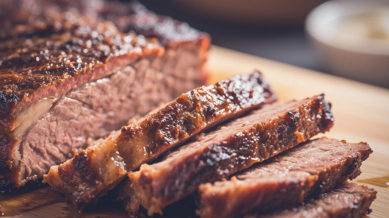 A glistening brisket cut into several slices on a wooden cutting board