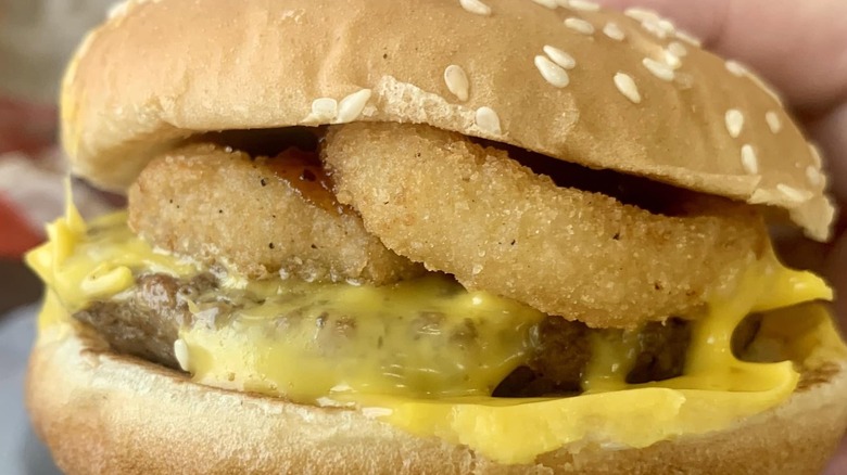 A cheeseburger with onion rings on it is shot close up.