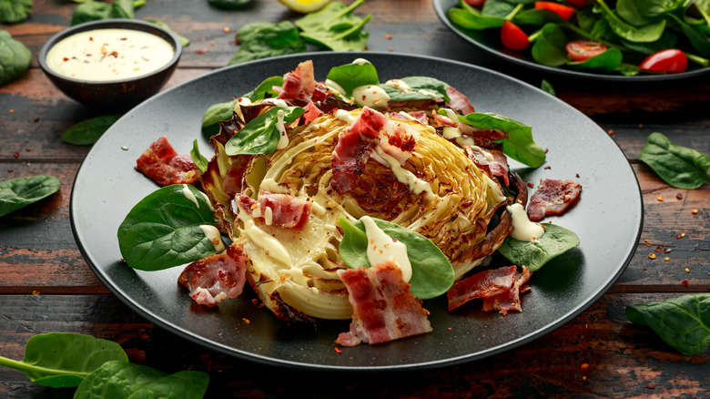 Overhead view of cooked cabbage wedge salad topped with greens, dressing, and bacon