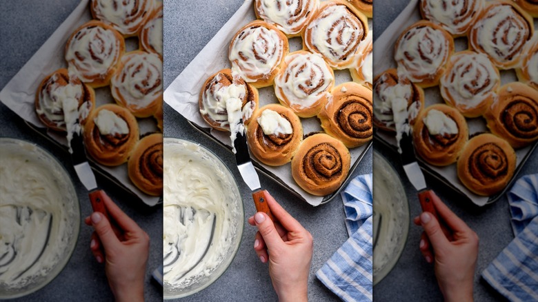 A person adding creamy frosting to cinnamon rolls