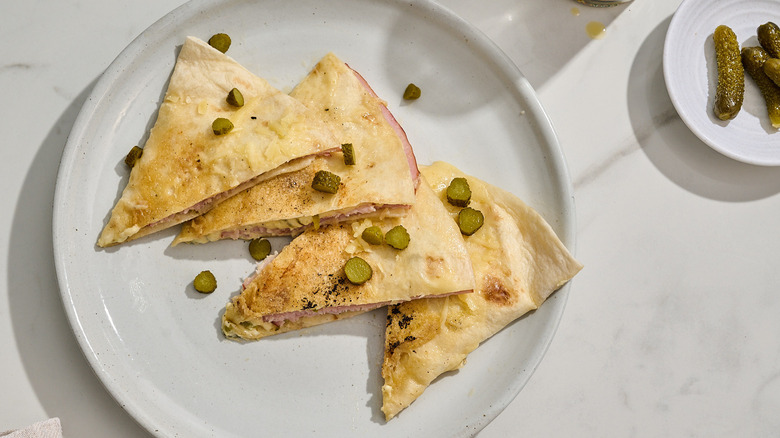 French-inspired quesadilla slices on a plate sprinkled with thinly sliced cornichons