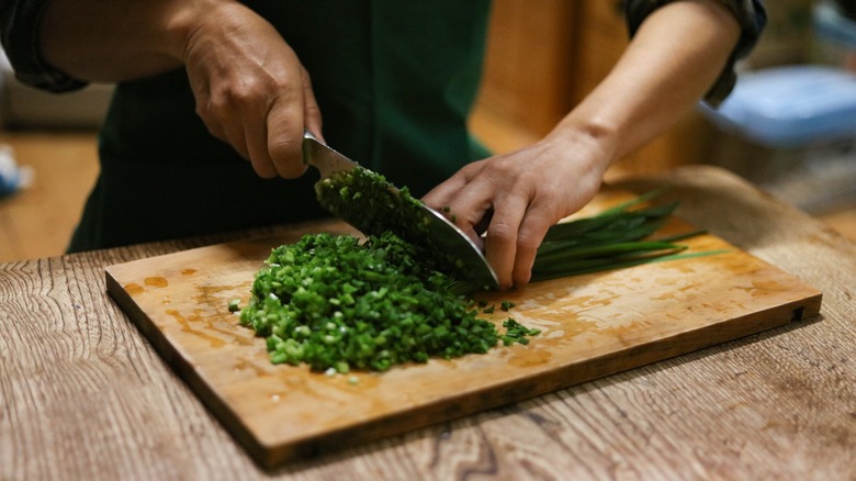 Petite hands chopping chives with chef's knife, wooden board