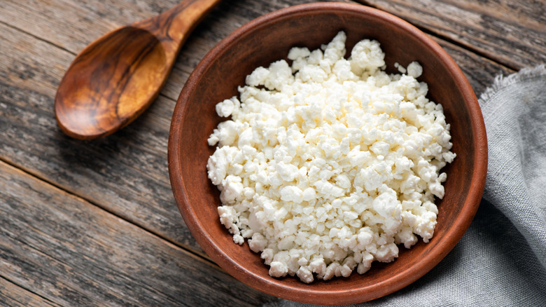 Bowl of cottage cheese on cutting board with wooden spoon.