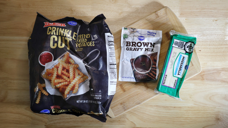 frozen crinkle cut fries, packet of brown gravy mix, and block of mozzarella cheese on a cutting board