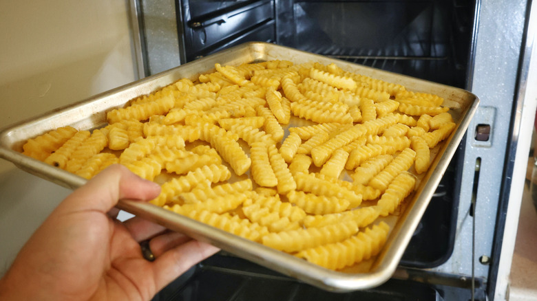 hand placing baking sheet of crinkle cut fries in the oven