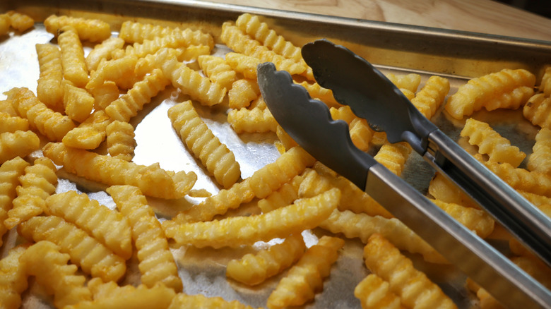baking sheet of crinkle cut fries with tongs laying on them