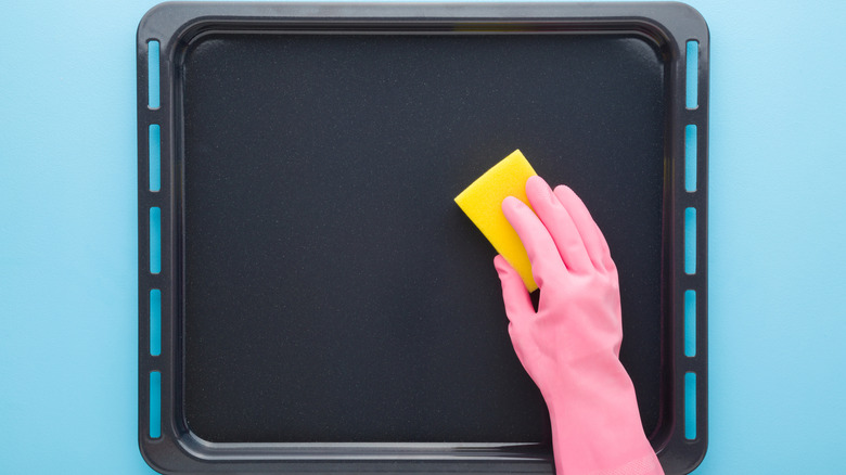Overhand view of gloved hand cleaning sheet pan