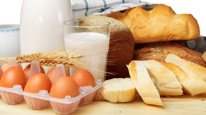 eggs, bread, milk, and wheat on a wooden countertop