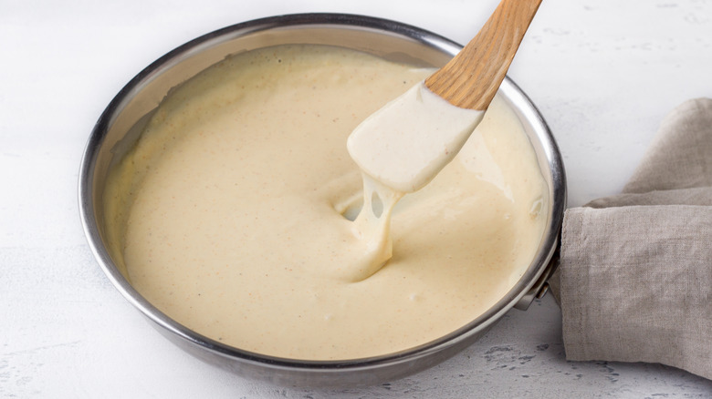 a wooden spatula lifting out of a skillet of creamy bechamel sauce