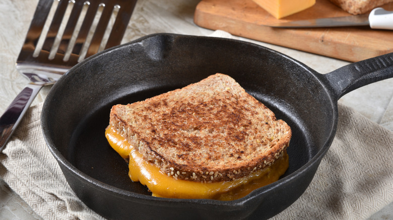 A grilled cheese sandwich in a cast iron pan on a towel next to a spatula