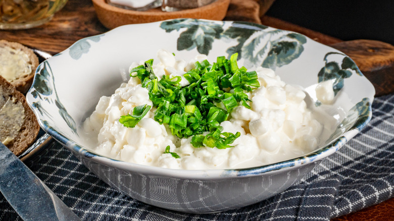 Cottage cheese with herbs on top in a white pottery bowl decorated with gray flowers.