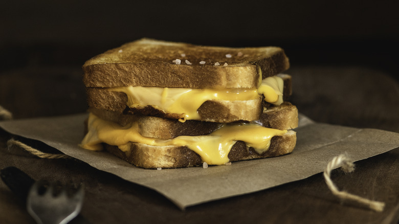 Two grilled cheese sandwiches stacked on one another atop brown paper, with yellow cheese oozing out of the sides.