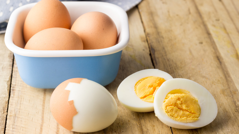 A small container of hard-boiled eggs sits beside two peeled and sliced hard-boiled eggs.