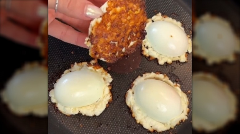 Four hard-boiled eggs are frying on a layer of feta cheese in a skillet.