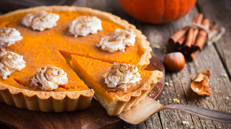 A pumpkin pie is topped with whipped cream and cinnamon, with one triangular slice cut out.