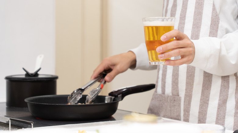 person cooks on stove while holding pint of beer
