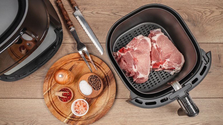 Two raw steaks in an air fryer basket next to bowls of seasonings