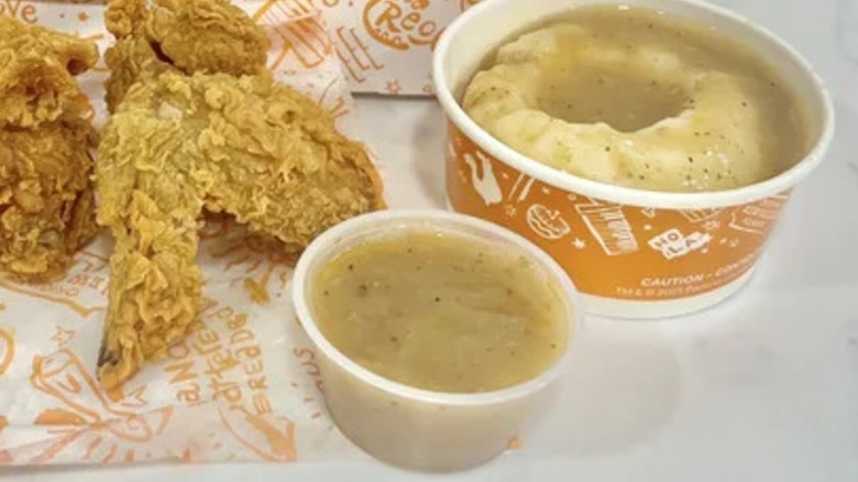 A side of Popeye's gravy next to some mashed potatoes and gravy and Popeye's chicken wings