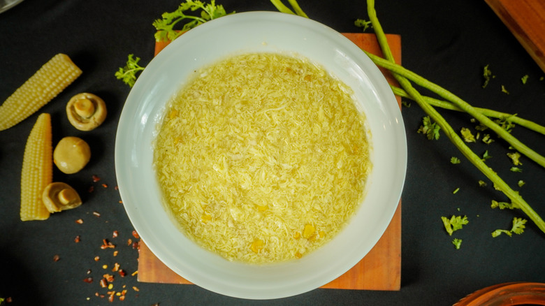 a bowl of soup with congealed egg proteins in it on a table surrounded by various raw vegetable ingredients