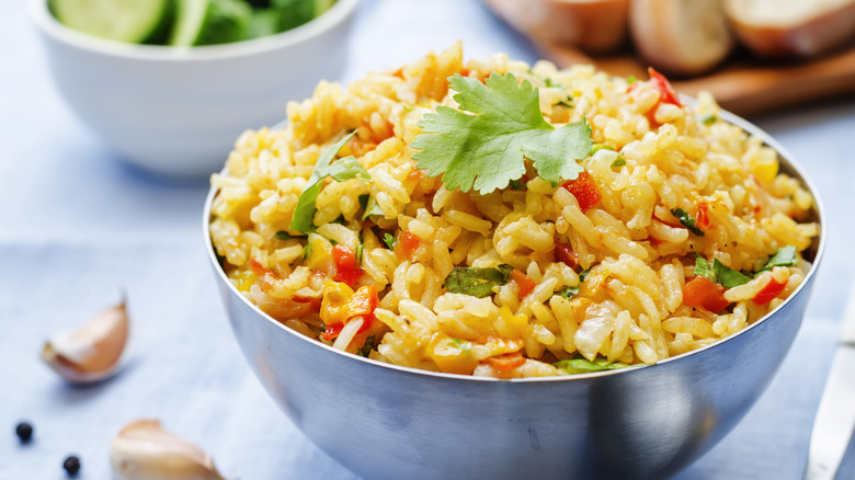 A small bowl of seasoned rice with vegetables next to cloves of garlic.