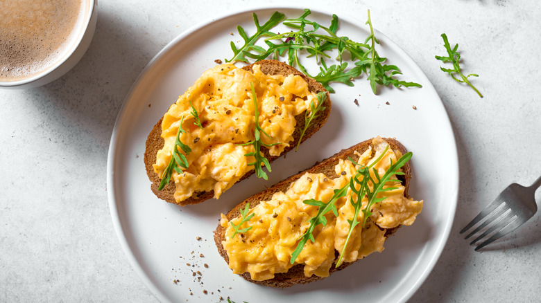 Two pieces of toast topped with bright scrambled eggs and fresh herbs