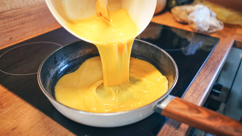A person pours raw scrambled eggs from a bowl into a pan