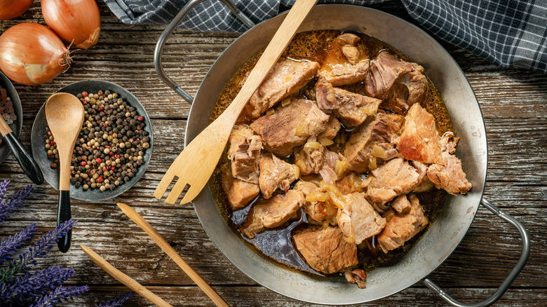 a pan of stewed pork with onions, herbs, and spices beside it