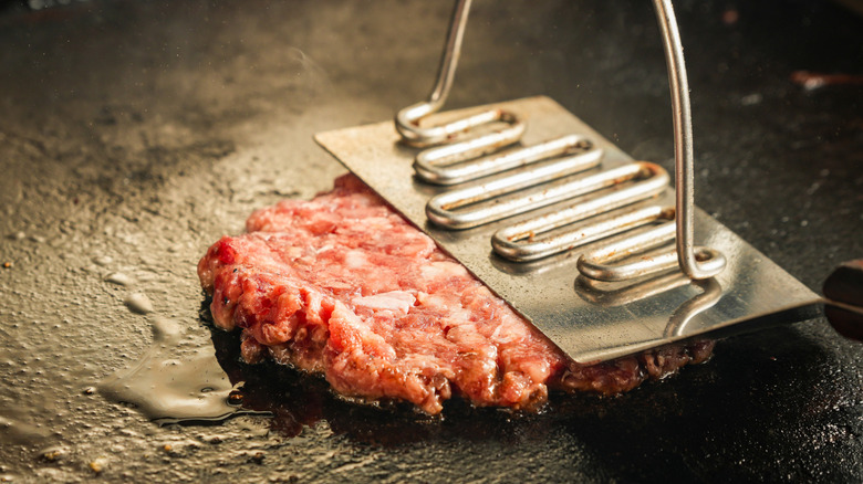 A smash burger being flattened on a griddle