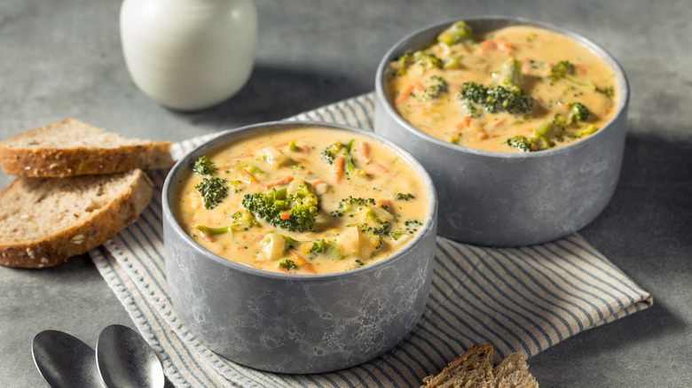 bowls of broccoli and cheese soup with slices of bread