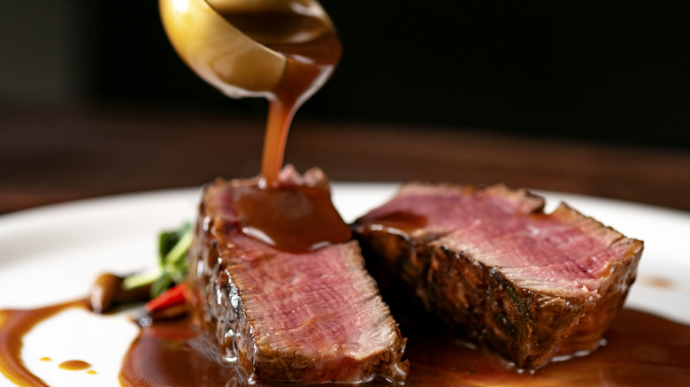 Sauce being poured from a ladle over a plated steak dinner
