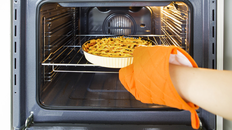 Foodie taking a warm apple pie out of a home oven