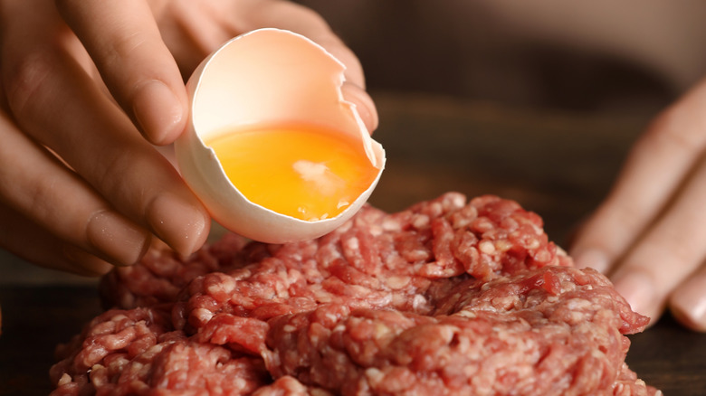 Hands pouring egg yolk from shell onto ground beef