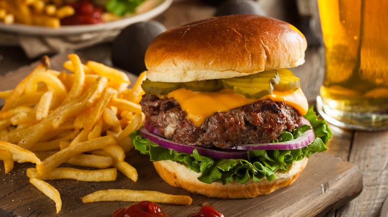 Cheeseburger with pickles, red onion, and lettuce, served on wooden board with French fries