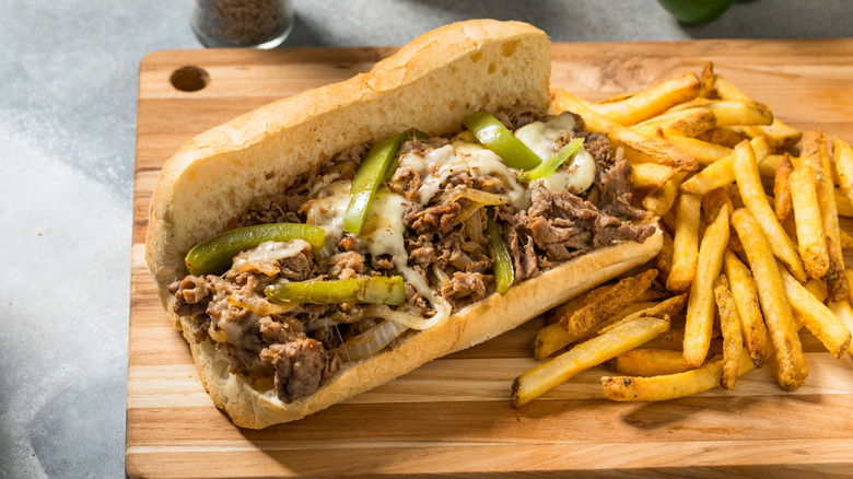 Cheesesteak sandwich with bell peppers on wooden cutting board with fries