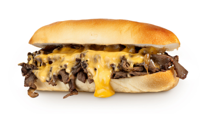 Cheesesteak sandwich with melted cheese on white background