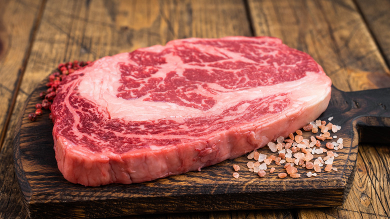 Fresh raw ribeye steak on wooden cutting board with salt