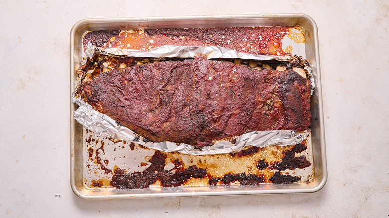 aerial view of baked ribs on a piece of foil over a dirty baking sheet