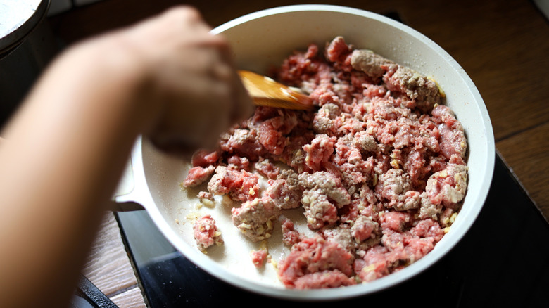 A person cooking ground beef in a pan