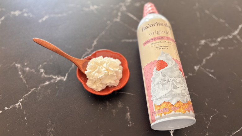 Can of Target brand whipped topping on a counter next to a bowl and spoon of whipped cream