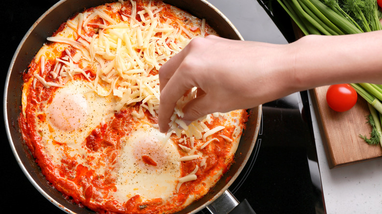 woman adding grated cheese to eggs alla pizzaiola