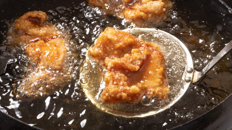 spoon scooping a fried chicken piece out of a pot of oil