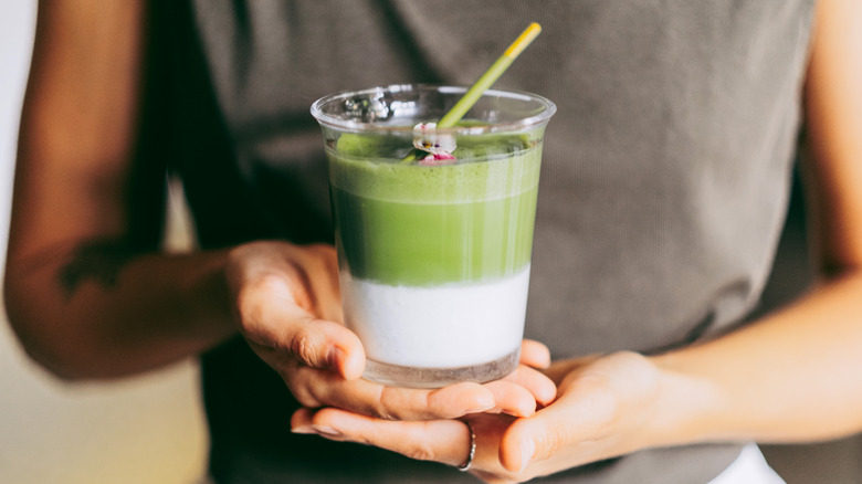A person holds a layered matcha beverage