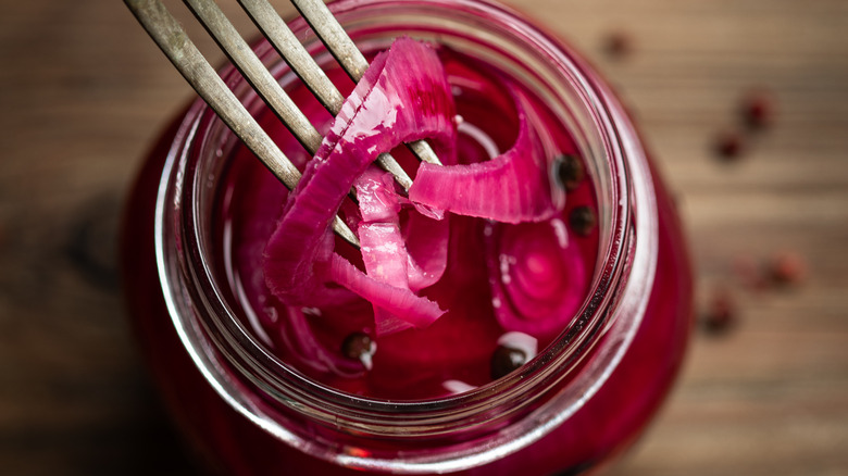 Fork plunging into mason jar of pickled red onions