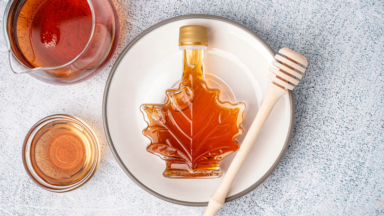 Maple syrup in maple leaf shaped bottle on plate with honey spoon and jug besides