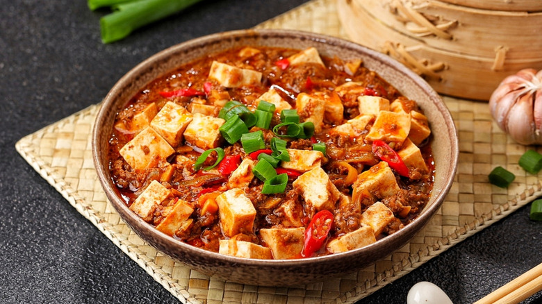 A bowl of mapo tofu garnished with scallions on a small mat