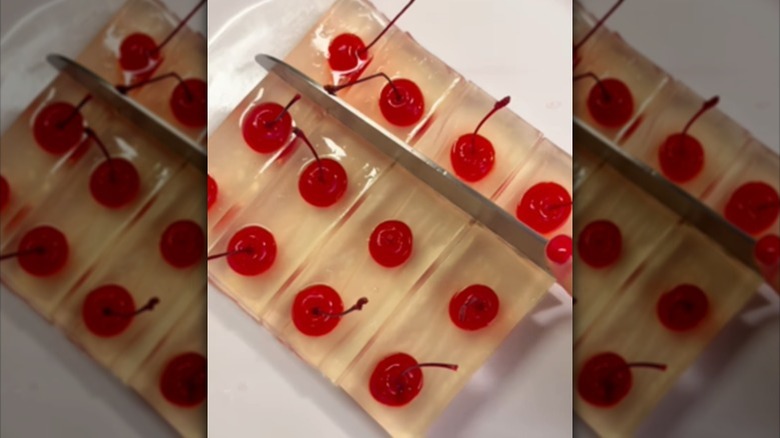 Set Jell-O shots with a cherry in each square being cut up with a large knife.