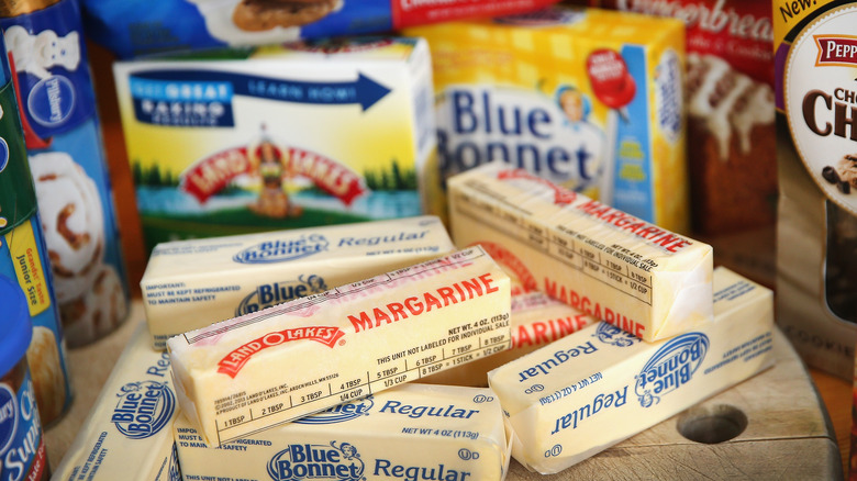 Sticks of margarine and regular butter centered on wooden tray around other packaged foods